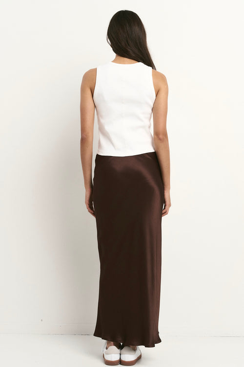 Woman wearing a chocolate brown satin midi skirt with a white tank and sneakers.