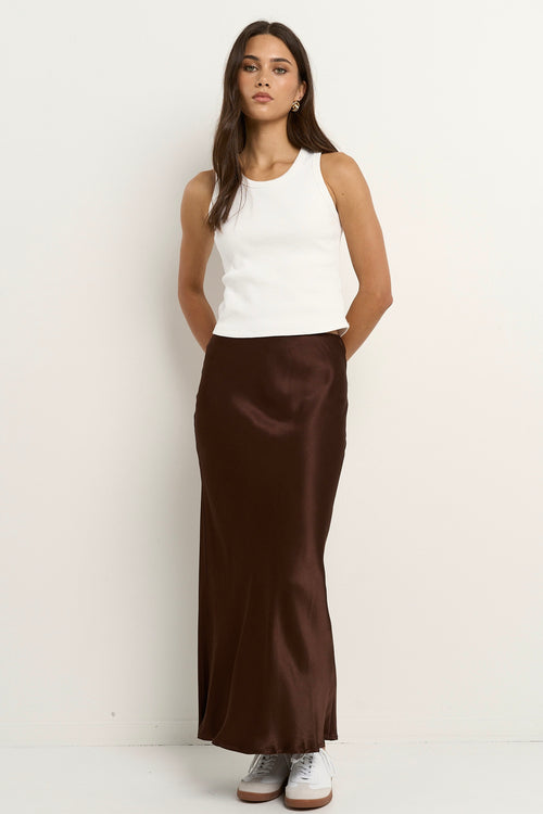 Woman wearing a chocolate brown satin midi skirt with a white tank and sneakers.