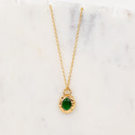 A gold chain necklace with an oval green gemstone pendant, displayed on a white marble surface.
