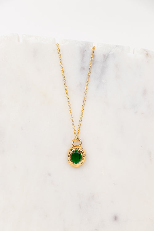 A gold chain necklace with an oval green gemstone pendant, displayed on a white marble surface.