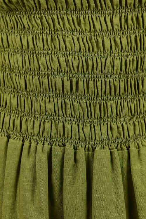 Close-up of an olive green smocked dress fabric, showing horizontal gathered bands and a pleated skirt section.