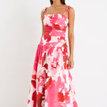 Woman wearing a floral pink and red ruched midi dress with tie-up straps and a flared hem, styled with minimal sandals.