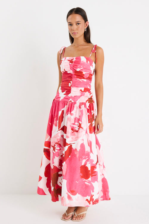 Woman wearing a floral pink and red ruched midi dress with tie-up straps and a flared hem, styled with minimal sandals.