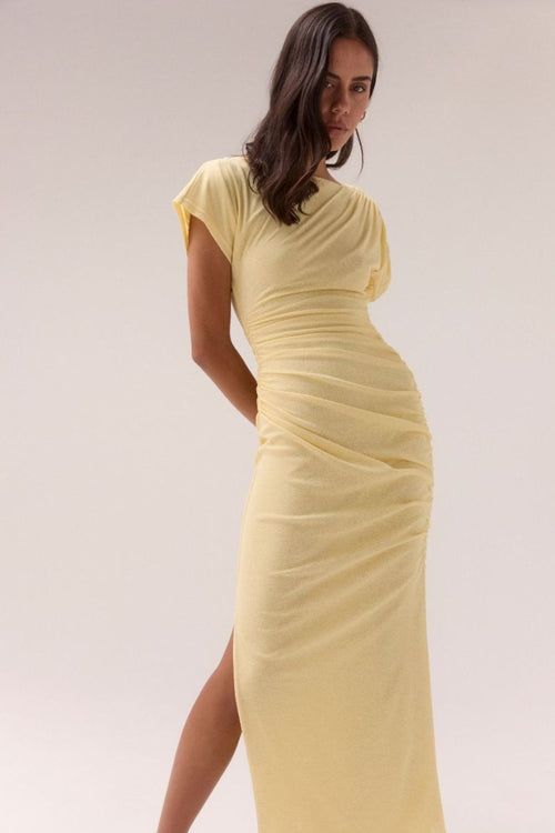 Lemon yellow maxi dress with short sleeves, ruched side detailing, high side slit, and a straight neckline, worn by a model in silver heels against a neutral background.