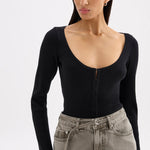 A woman wearing a black ribbed long-sleeve scoop-neck top with a front zipper, paired with gray high-waisted jeans, against a plain light gray background.
