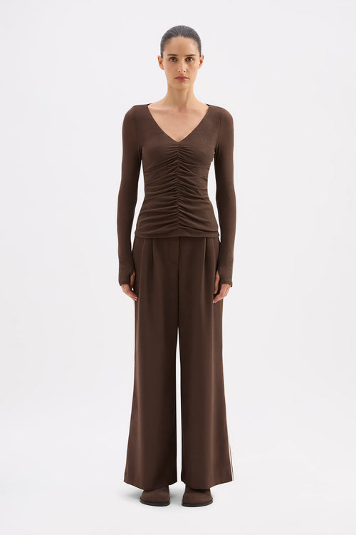 Woman wearing a brown ruched top and wide-leg pants on a white background