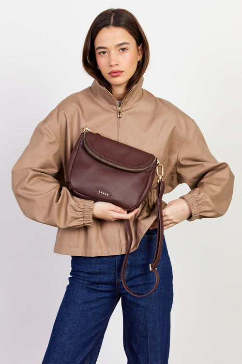Woman holding a brown leather bag against a plain background