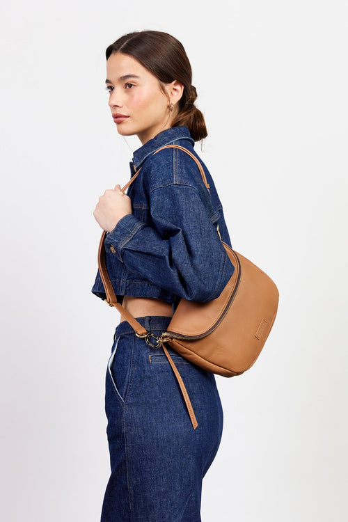 Woman wearing a denim jacket and jeans with a brown leather bag on a white background