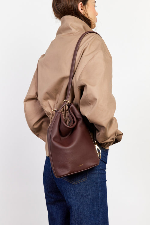 Person wearing a brown leather bag over their shoulder against a plain background