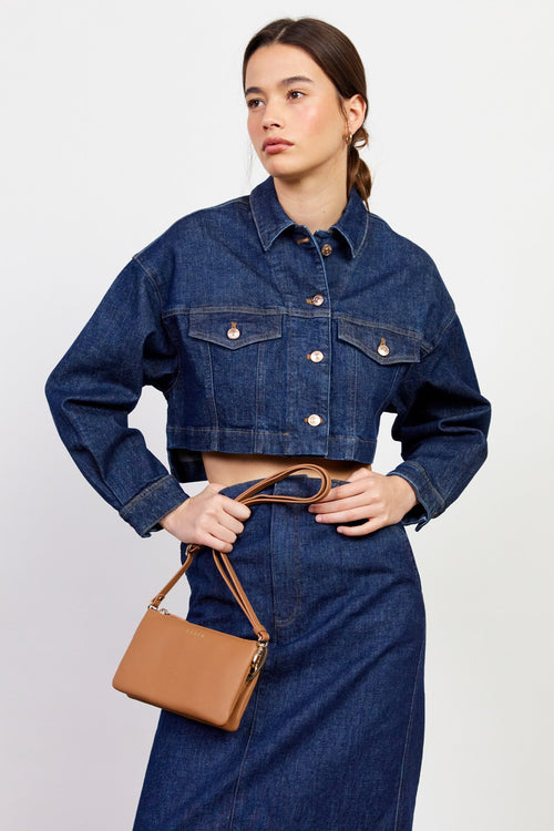 Person wearing a blue denim jacket and holding a brown handbag on a white background