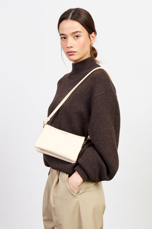 Woman wearing a brown sweater with a beige crossbody bag on a white background