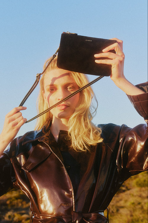 Person holding a black clutch with a strap over their face against a blue sky.