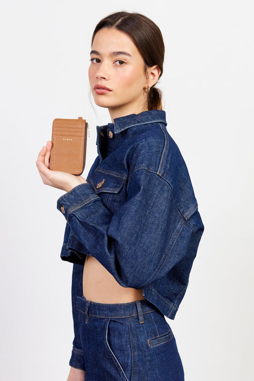 Woman wearing a blue denim jacket holding a brown wallet against a white background