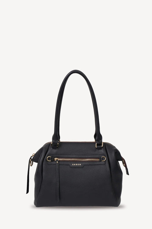 A black leather handbag with gold-tone hardware, featuring dual top handles, a front zippered pocket, and a small gold KAWS logo plaque on the front, set against a plain off-white background.