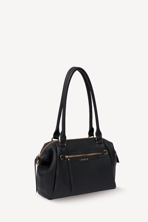 A black leather handbag with gold-tone hardware and a front zip pocket, shown on a clean off-white background.