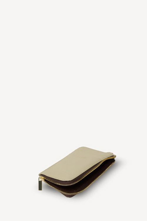 A slim, zippered pouch or wallet in light beige leather with gold-tone hardware, shown open against a solid off-white background.