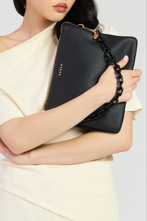 Woman holding a black clutch with a chain detail against a light background