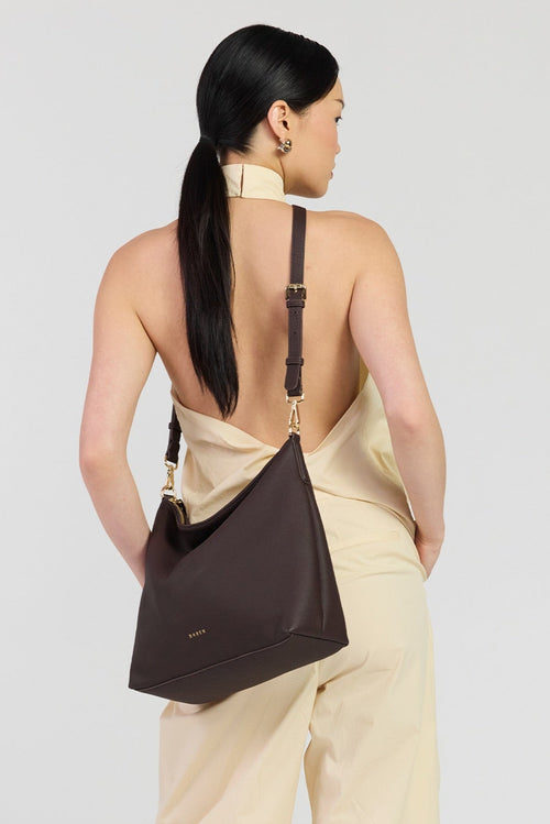 Woman wearing a brown shoulder bag on a plain background