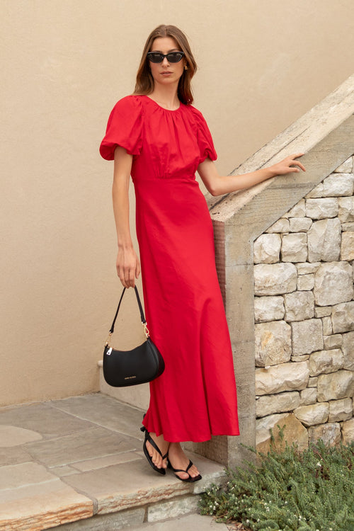 Woman in a red dress standing against a beige wall with stone steps.