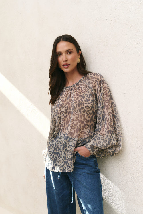 Woman wearing a leopard print blouse and blue jeans against a light background