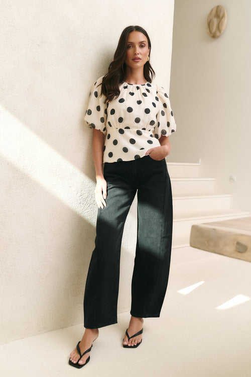 Woman wearing a polka dot top and dark pants in a bright indoor setting