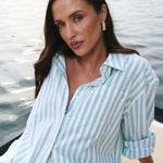 Woman wearing a light blue and white striped shirt by a body of water.