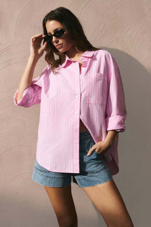 Woman wearing a pink shirt and denim shorts against a beige wall