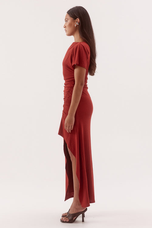 A woman in profile wearing a fitted, short-sleeve red dress with puff sleeves and a high slit, standing against a plain light background.