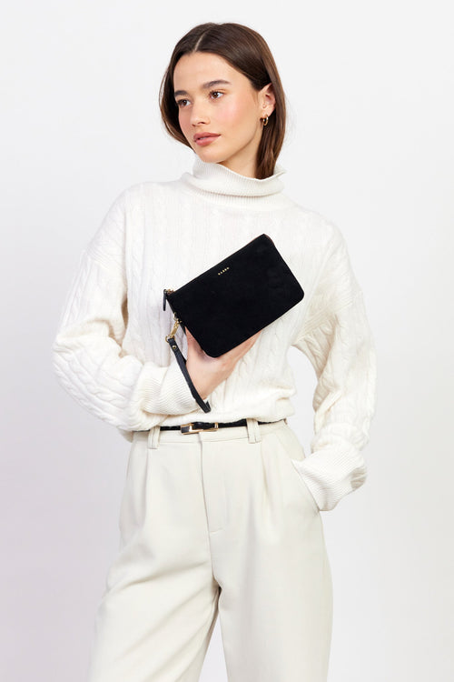 Woman in a white outfit holding a black clutch against a plain background