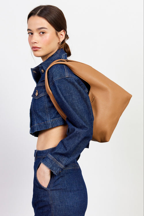 Woman wearing a denim outfit with a brown tote bag on a white background