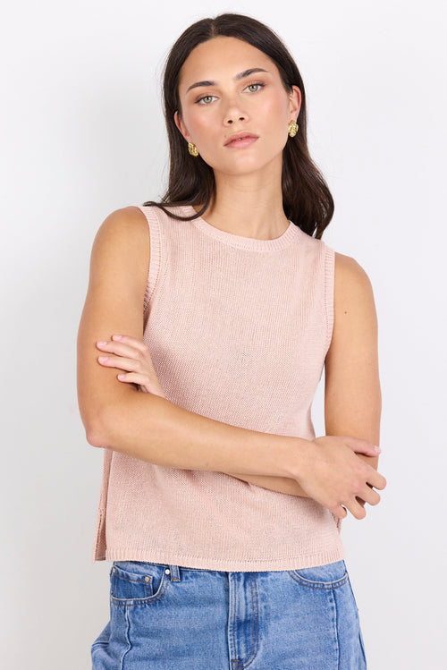 Woman wearing a light pink sleeveless top and blue jeans against a white background