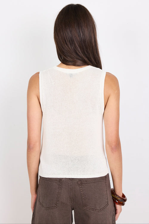 Woman wearing a white knit sleeveless top against a plain background