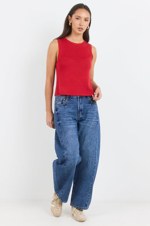 Woman wearing a red sleeveless top and blue jeans on a white background
