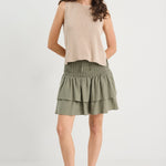 Woman wearing a beige sleeveless top and green skirt on a white background