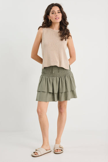 Woman wearing a beige sleeveless top and green skirt on a white background