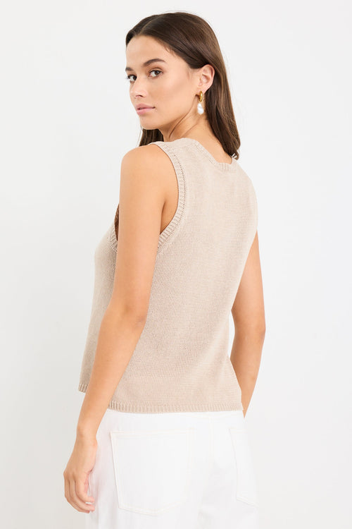 Woman wearing a sleeveless sand-colored knit tank top with a crew neckline and relaxed fit, paired with high-waisted white jeans.