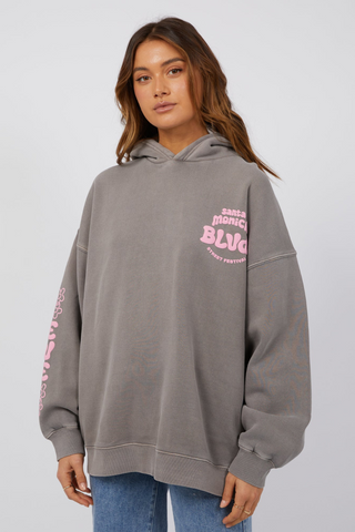 model wearing grey hoodie with pink lettering and blue jeans