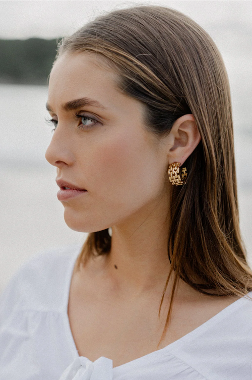 A pair of gold-toned hoop earrings featuring an intricate woven-link design, creating a bold, structured look with a glossy finish and open-back detail