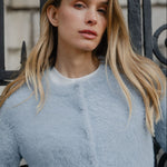 Woman wearing a light blue fuzzy sweater in front of an iron gate.