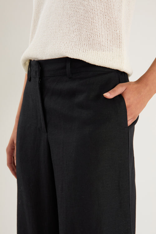 Person wearing black pants and a light-colored sweater on a plain background