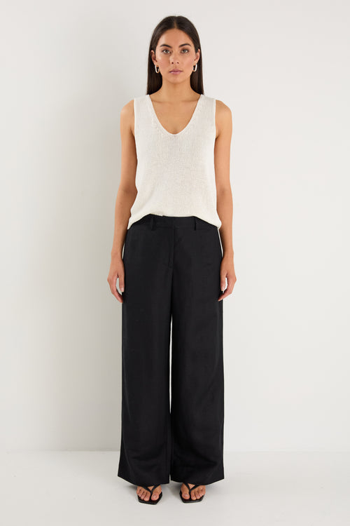 Woman wearing a white sleeveless top and black pants on a white background