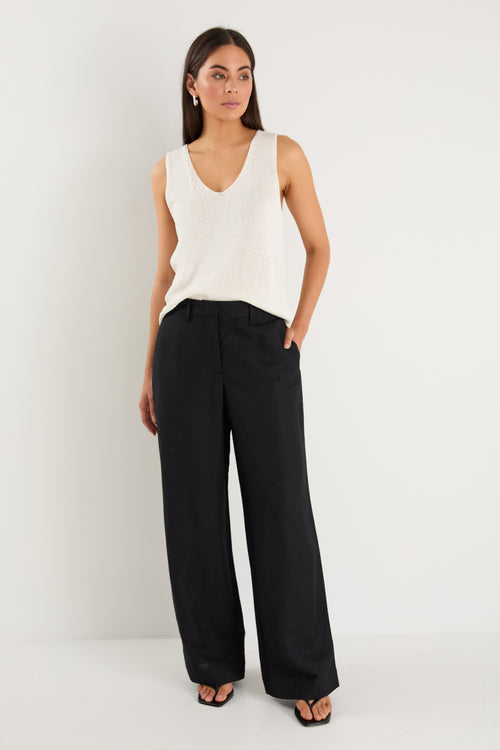 Woman wearing a white sleeveless top and black wide-leg pants on a white background