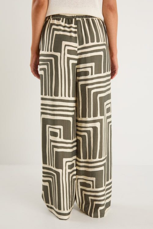 Woman wearing high-rise, wide-leg pants with an abstract khaki and ivory geo print and elasticated waistband with drawstring.