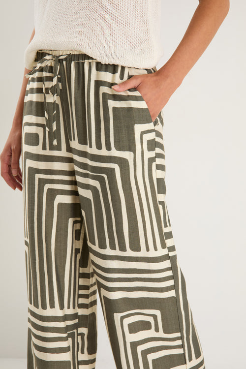 Woman wearing high-rise, wide-leg pants with an abstract khaki and ivory geo print and elasticated waistband with drawstring.
