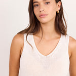 A woman with long brown hair wearing a cream-colored, textured knit sleeveless tank top, photographed against a plain light background.