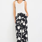 Woman wearing a white sleeveless top and black floral pants on a white background