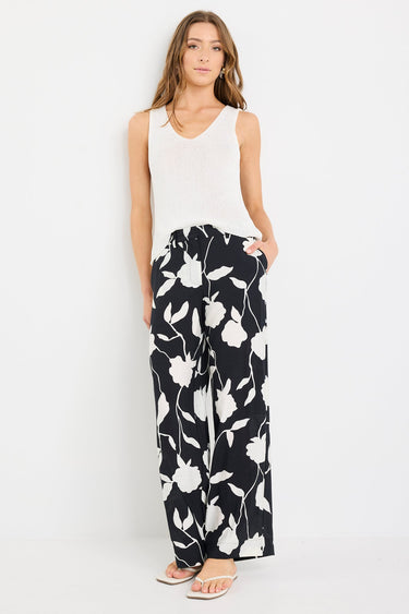 Woman wearing a white sleeveless top and black floral pants on a white background