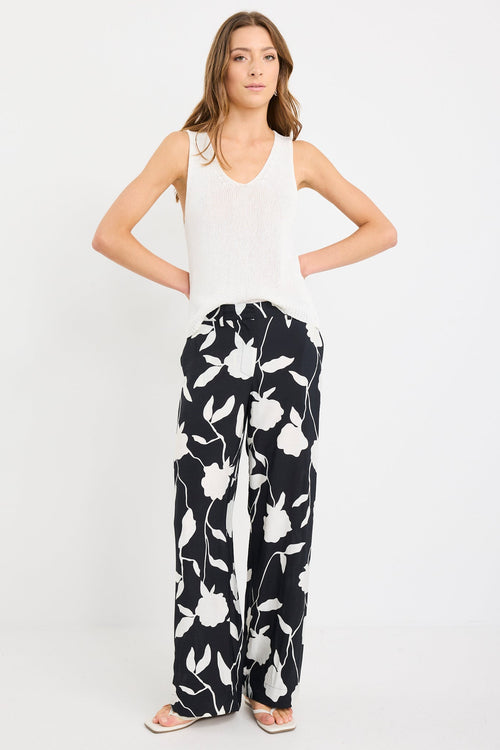 Woman wearing a white sleeveless top and black floral pants on a white background