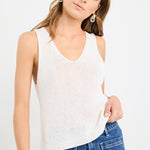 Woman wearing an ivory sleeveless knit vest top with a V-neckline, styled casually with blue jeans.