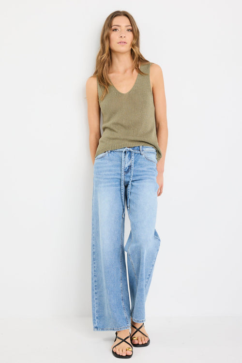 Woman wearing a sleeveless khaki knit top with a V neckline and relaxed fit, styled with light blue jeans.